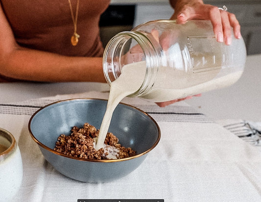 Woman pouring homemade cashew milk into granola bowl